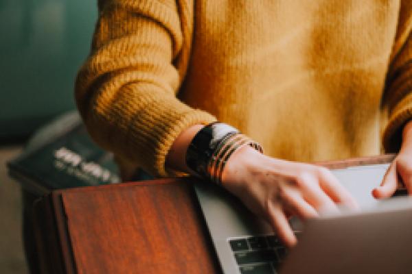 person in an gold colored sweater typing on a laptop